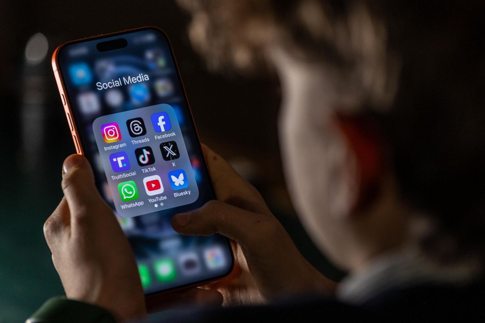 14-year-old boy holding an iPhone screen displaying several social media apps