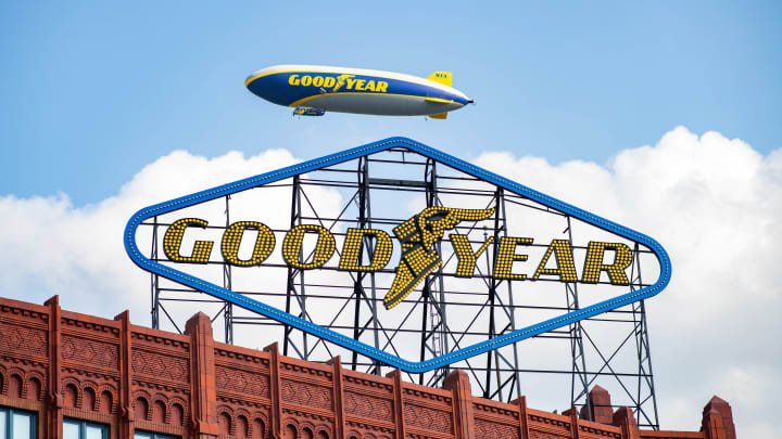 A Goodyear blimp flies behind a historic sign for the company in Akron, Ohio.