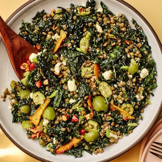 A big kale and lentil salad in a serving bowl with torn olives and strips of lemon peel.