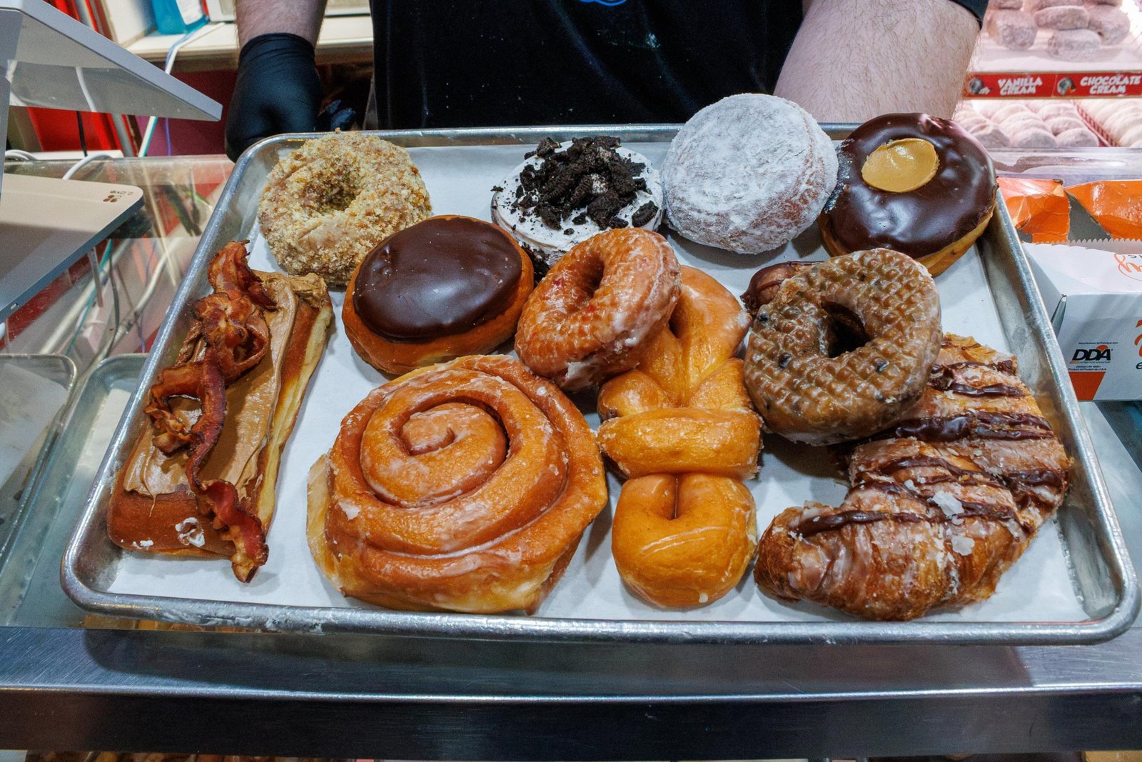 a tray of donuts including maple bacon, chocolate, strawberry, cinnamon, a cronut, a buckeye donut, and more