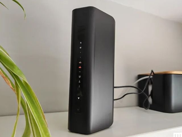 Netgear Nighthawk RS300 wifi router a black narrow device sitting on a white shelf with 2 wires coming from the back