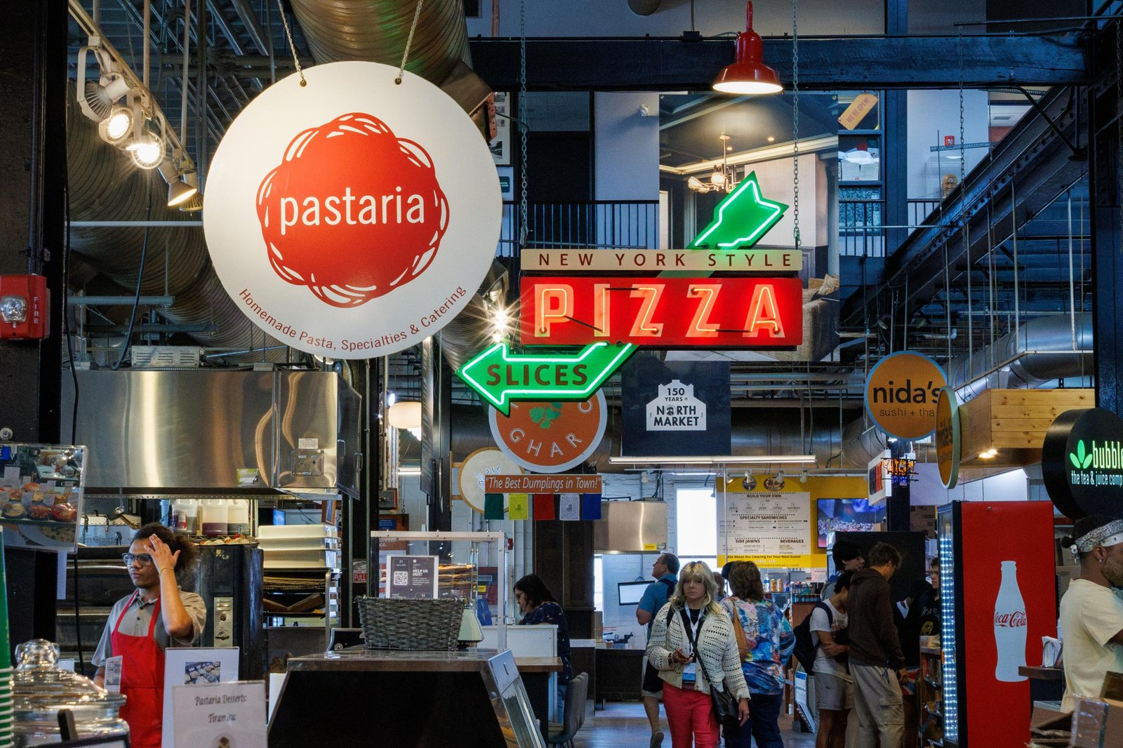 restaurant signs suspended over the walkway of the north market food hall in columbus, ohio, including one for pastaria and one that says pizza