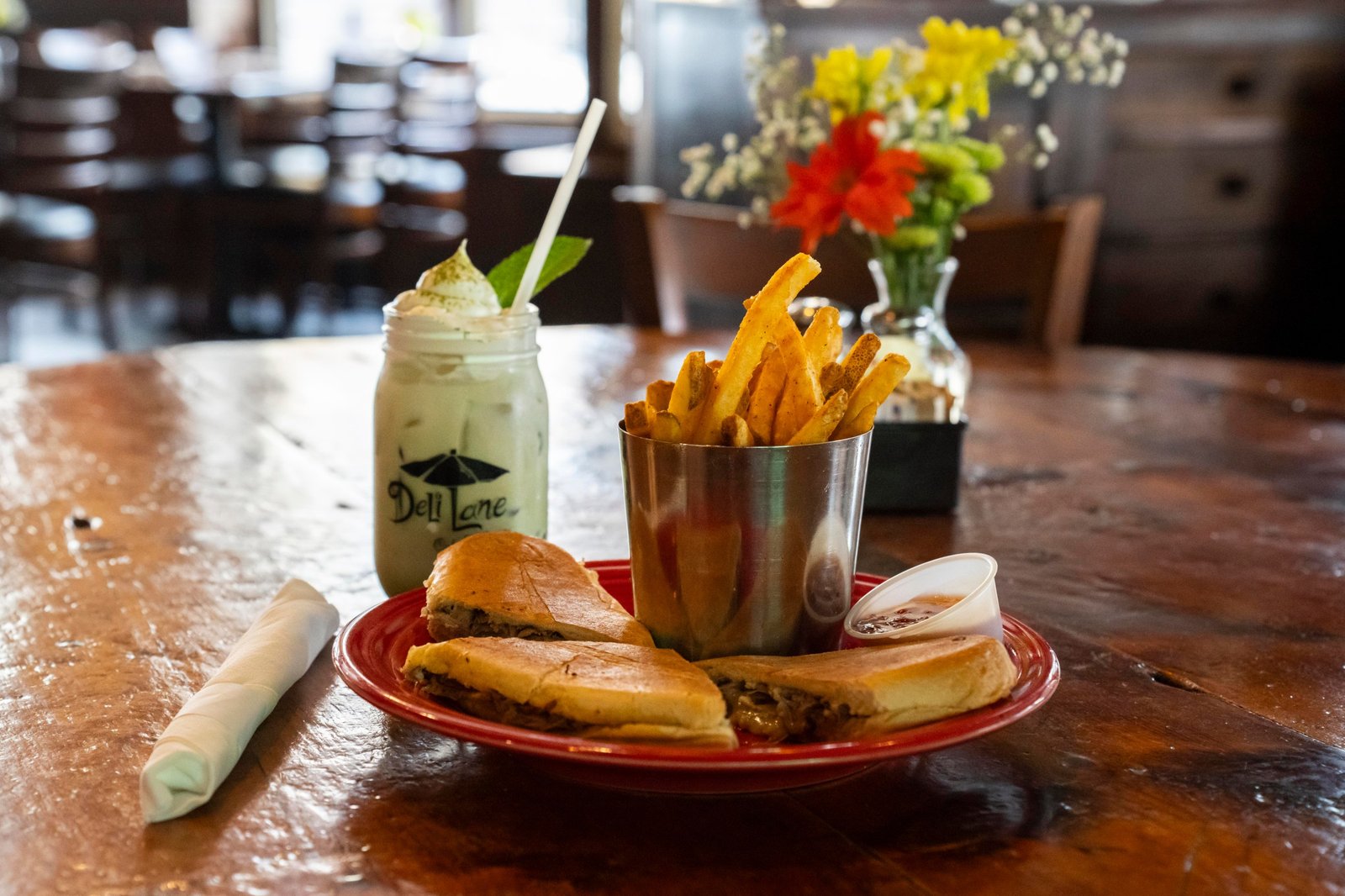 A sandwich and fries on a plate and a matcha latte in a jar on a restaurant table.