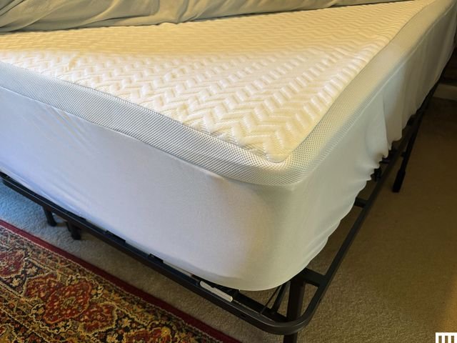 Closeup corner view of The Company Store Serene Foam Memory Foam Topper a white pad on top of a thick mattress