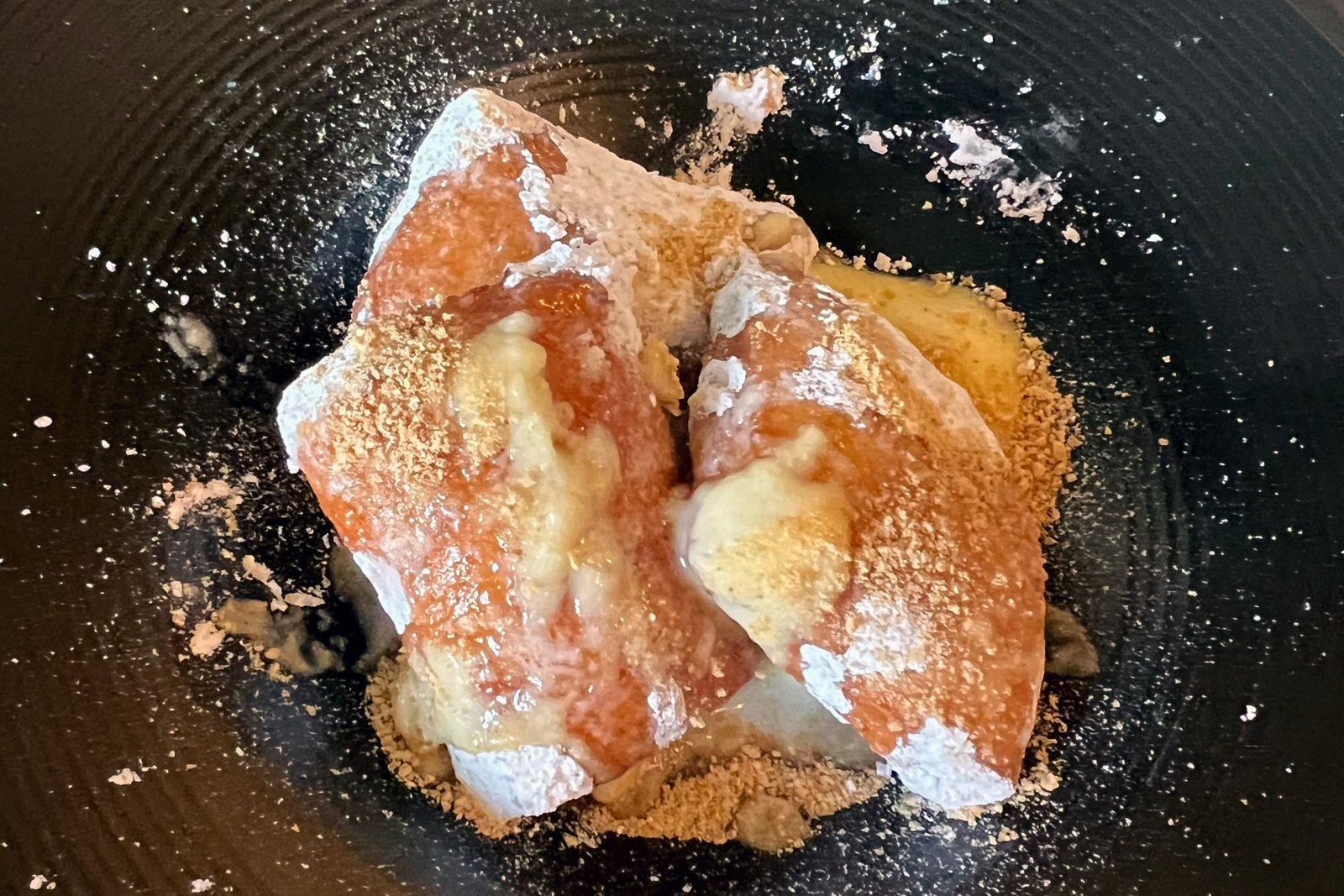 Three beignets covered in powdered sugar and leaking custard.