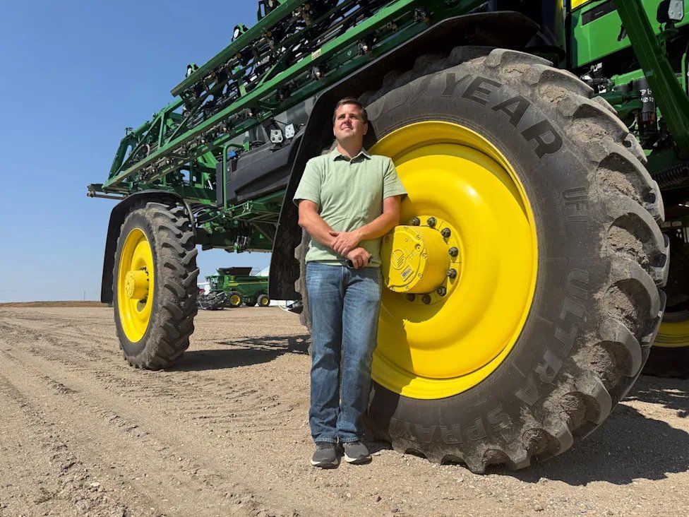 Dean Roberts, who grows crops including canola, wheat, barley and lentils on his farm in Coleville, Sask., stands next one of his farm rigs. Roberts says Canada is lagging behind competitor nations in technological adoption, which other experts say is key to boosting agri-food exports. (Emma Godmere/CBC - image credit)
