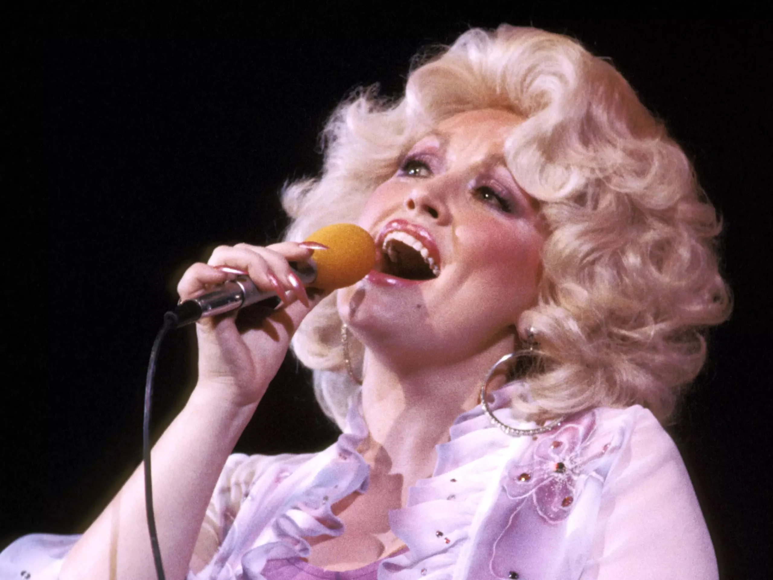 Dolly Parton sings into a microphone that she's holding.
