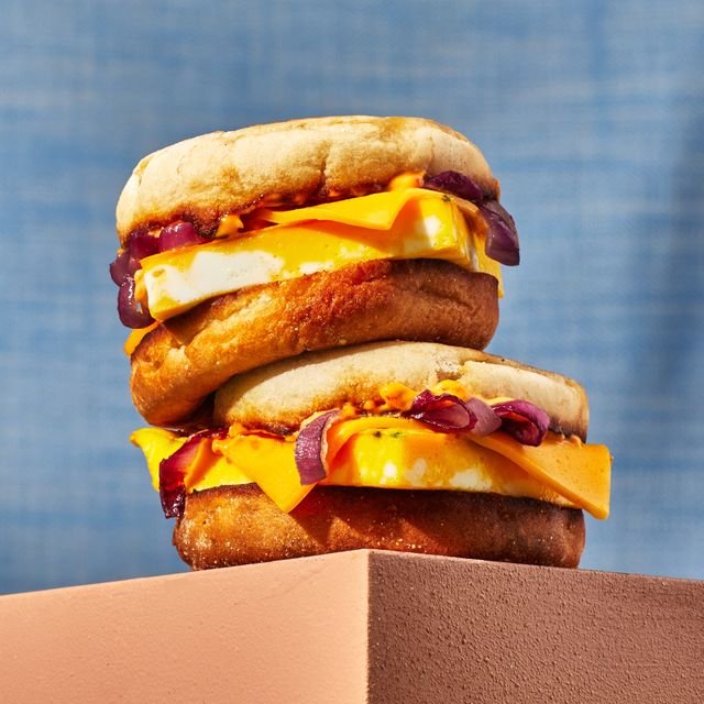 Two egg and cheese breakfast sandwiches on English muffins stacked on a wooden table.