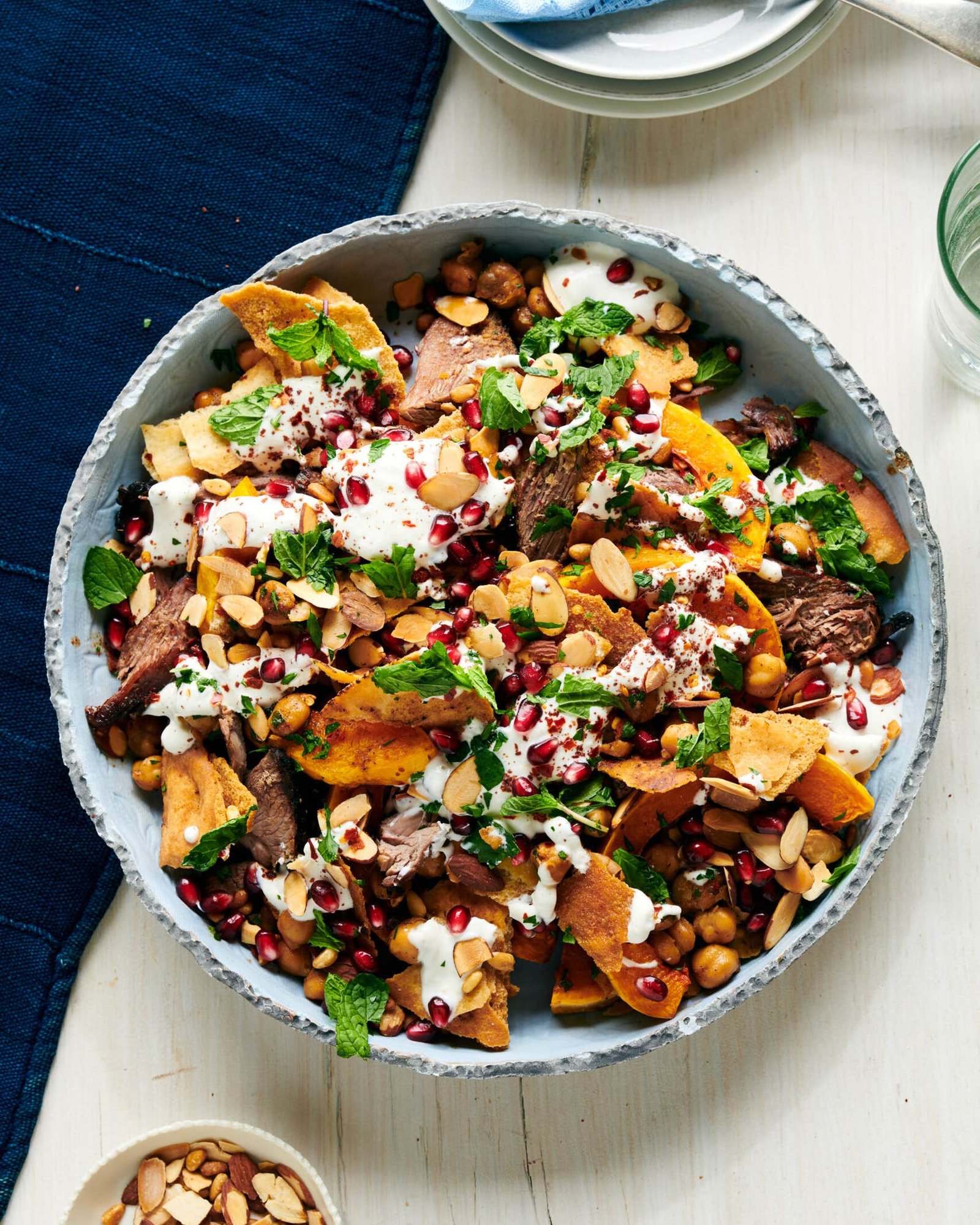 Lamb and Squash Fatteh With Tahini-Yogurt Sauce Lamb and squash fatteh in a shallow bowl, layered with chickpeas and pita chips and topped with tahini-yogurt sauce, sliced almonds, herbs, and pomegranate seeds.