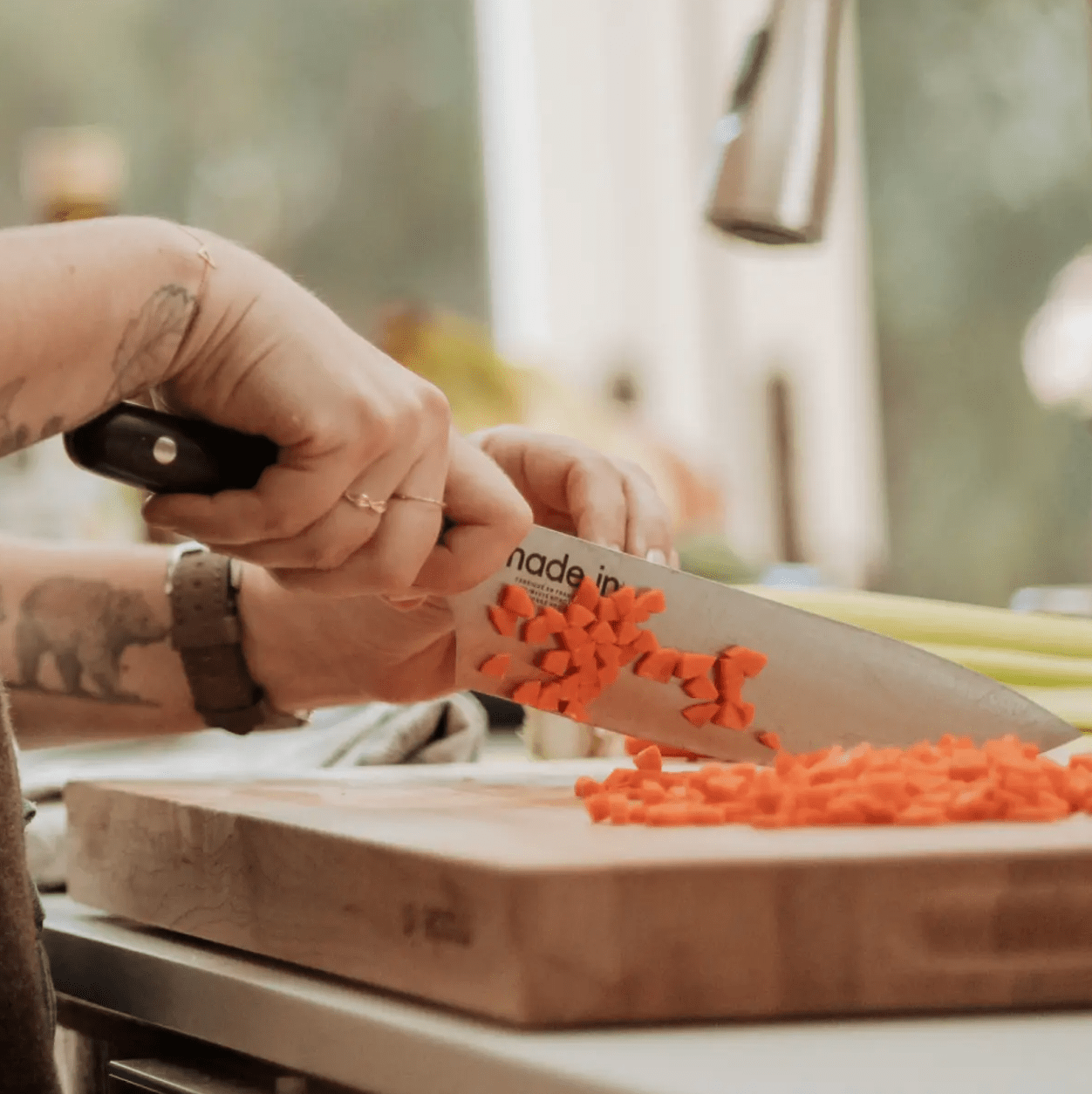 hands using a knife to chop carrots on a counter.