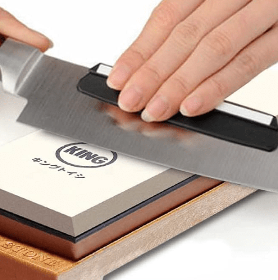 hands holding a knife being sharpened on a whetstone.