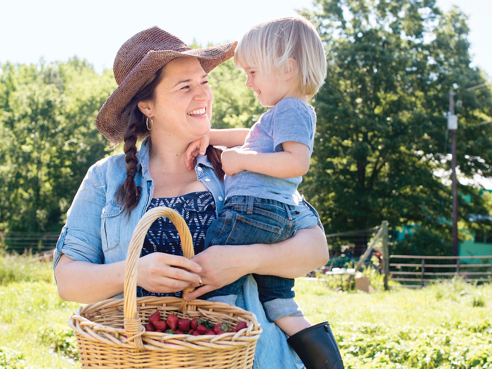 Middle of Somewhere A smiling farmer holds a child and a basket of freshly picked strawberries in a sunny field.