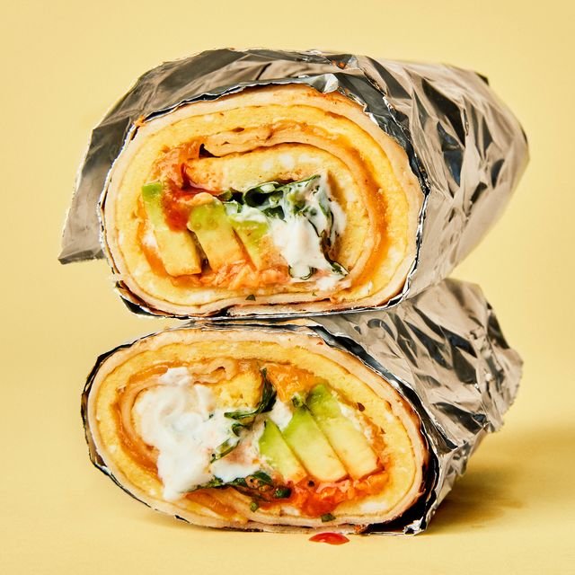A breakfast burrito with scrambled eggs and avocado wrapped in foil cut in half and stacked revealing the cut edge.
