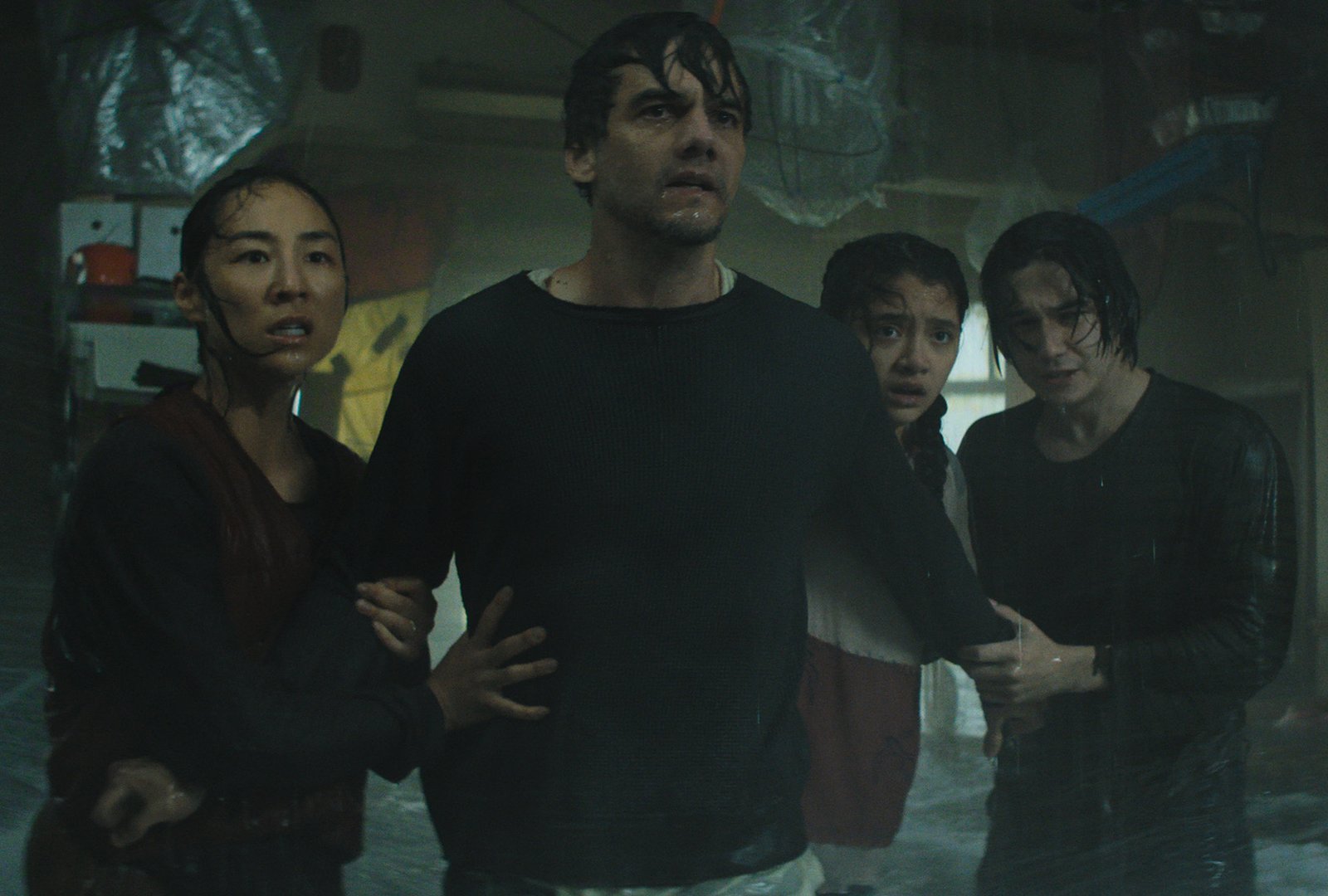 A family of four stands close together in a dark, water-damaged room, their clothes soaked and expressions fearful, in a scene from "The Last House."