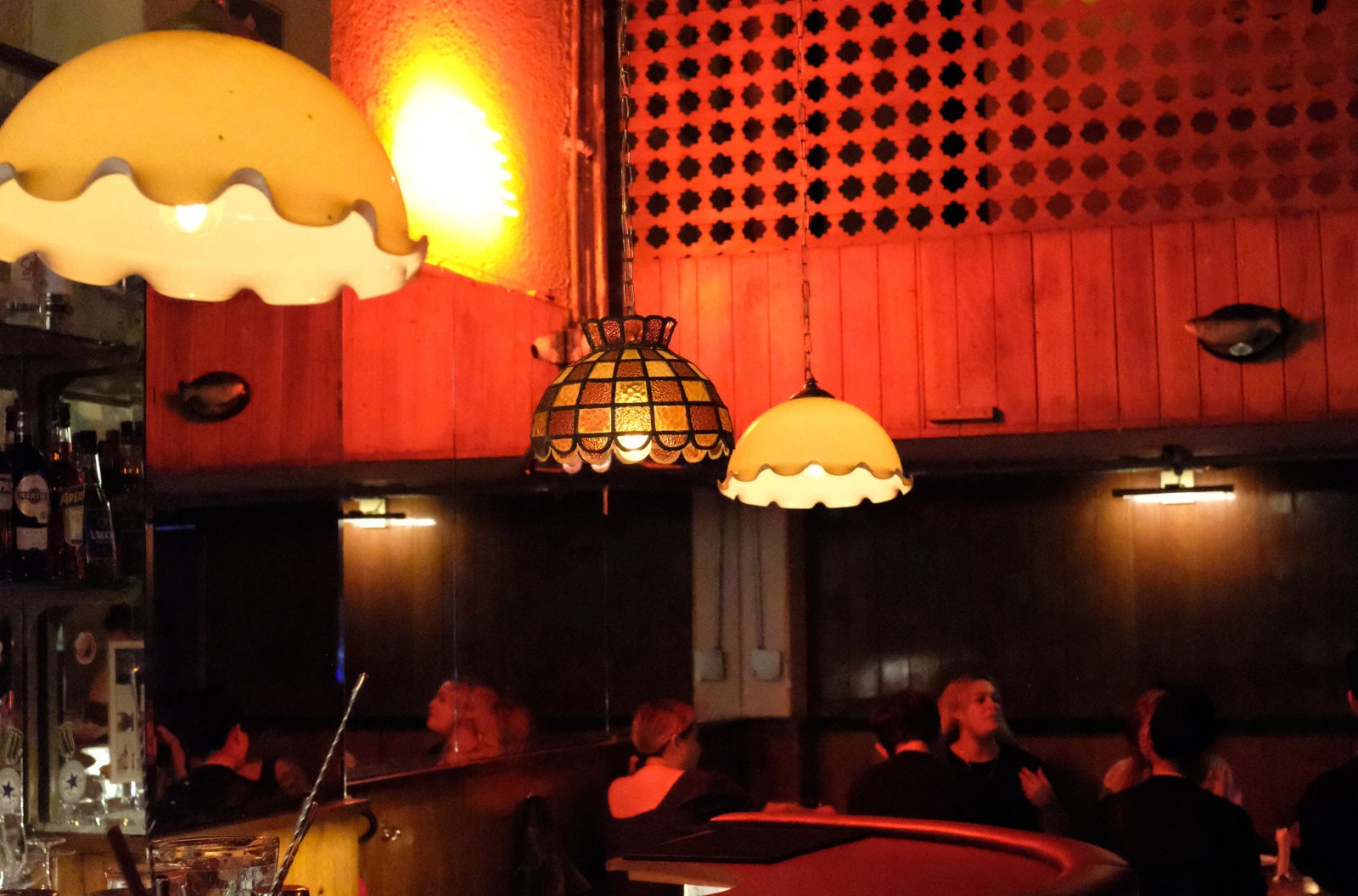 A dark, red-lit bar with antique pendant lights over a curved wood bar and diners seated at booths in the dark.