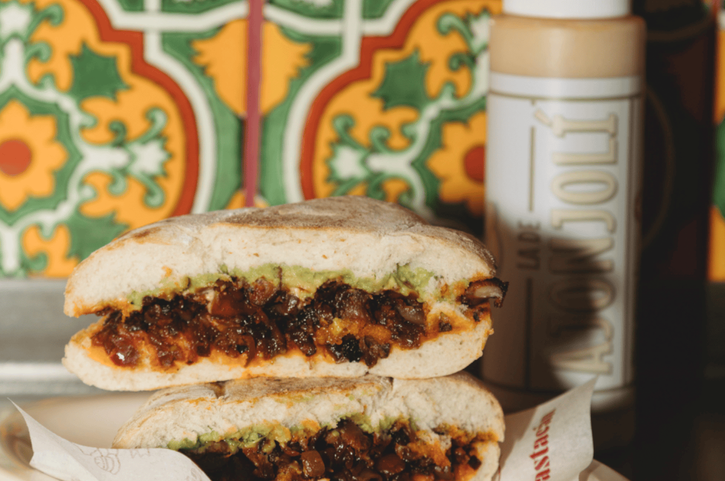 A torta, sliced in half and stacked, on a counter beside a squeeze bottle of sauce and decorative wall tiles.