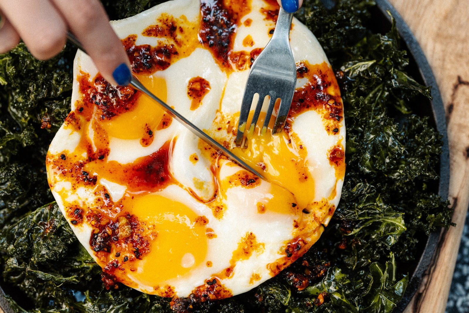 A diner cuts into fried eggs topped with streaks of red salsa.