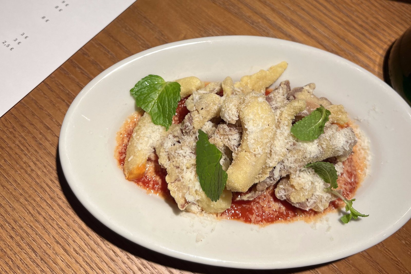 Slices of fried tripe covered in grated cheese, sitting a pool of tomato sauce.