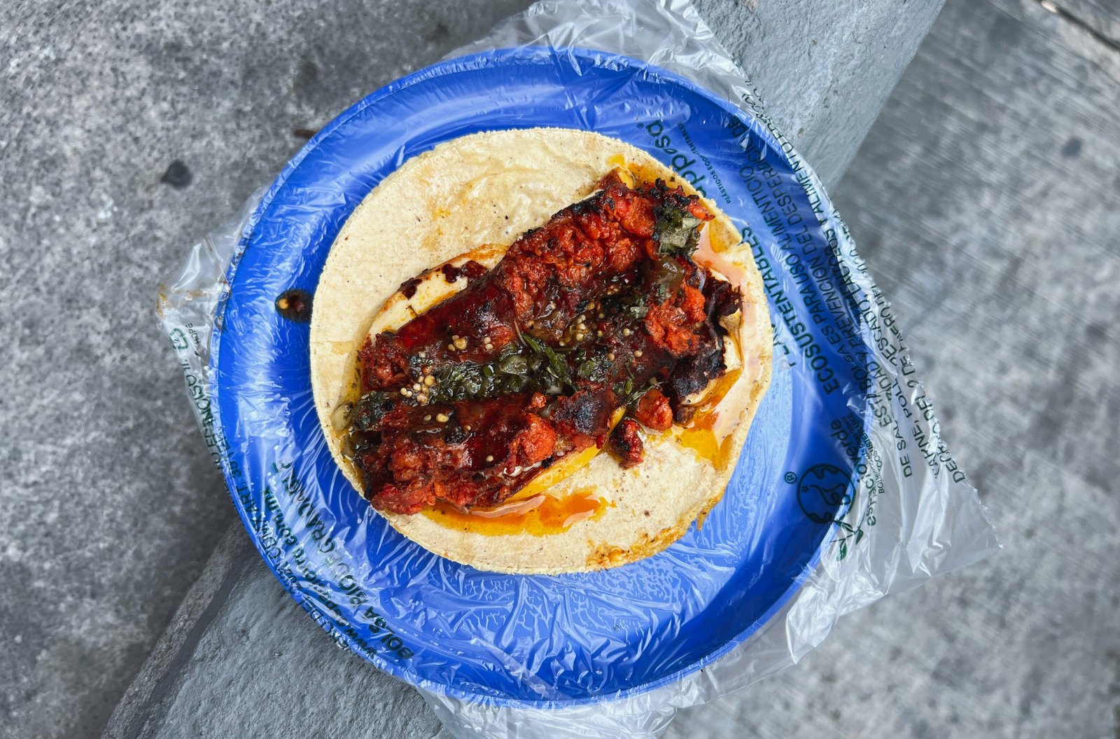 A taco on a plastic-wrapped plate, topped with deep red stewy meat.