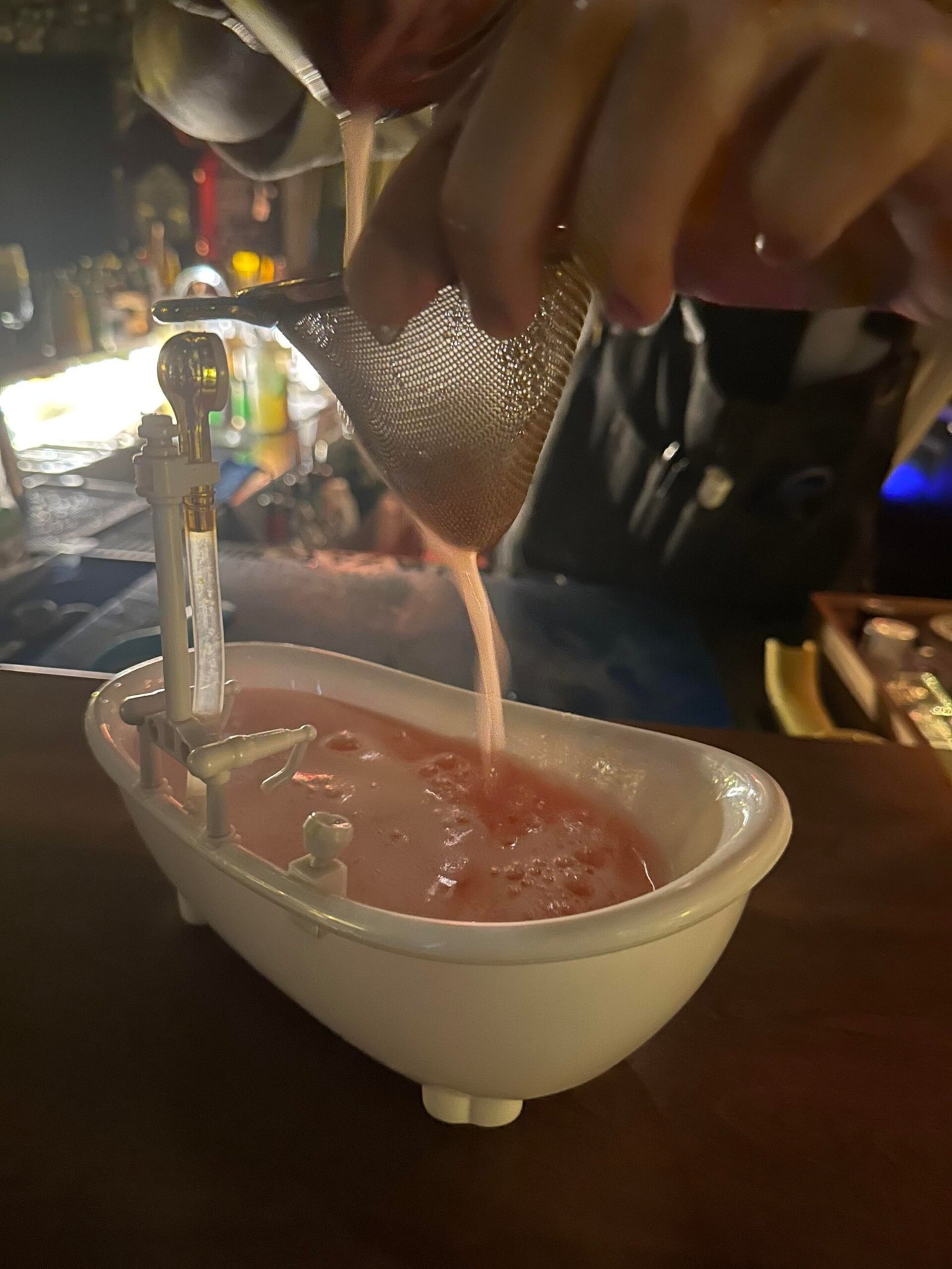 A pink cocktail is poured into a bathtub-shaped cup.