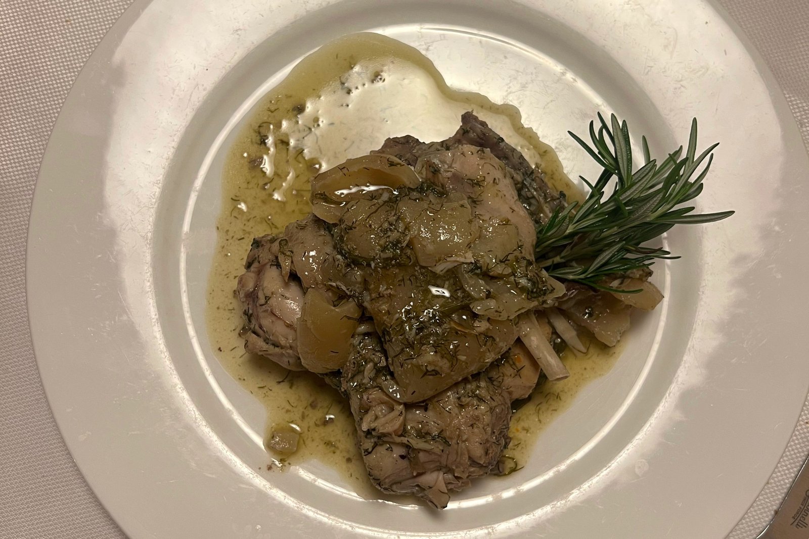 A meaty dish with a sprig of green garnish on a white plate.