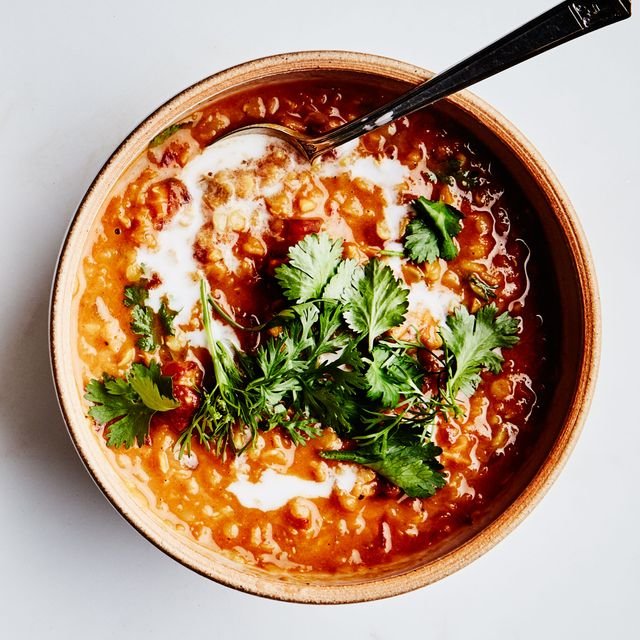 Two bowls of bright orange curry lentil soup topped with coconut milk and cilantro.