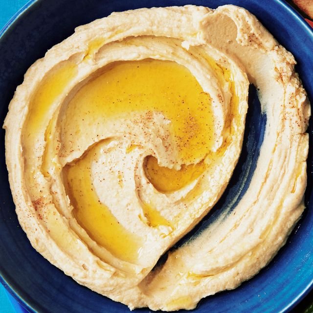 A serving bowl of hummus topped with olive oil and paprika with a swipe run through it as from a carrot.