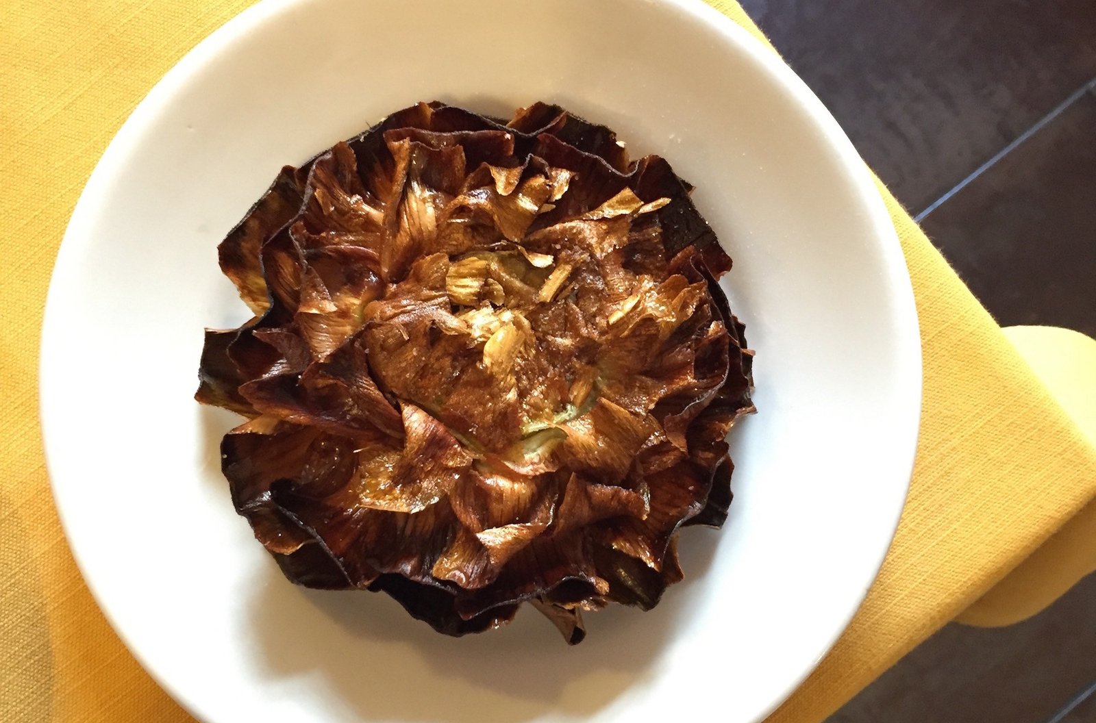 A large fried artichoke on a plate, on the corner of a table.